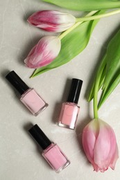 Flat lay composition with pink nail polishes in bottles and tulip flowers on light textured table