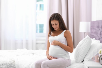 Happy pregnant woman sitting on bed at home