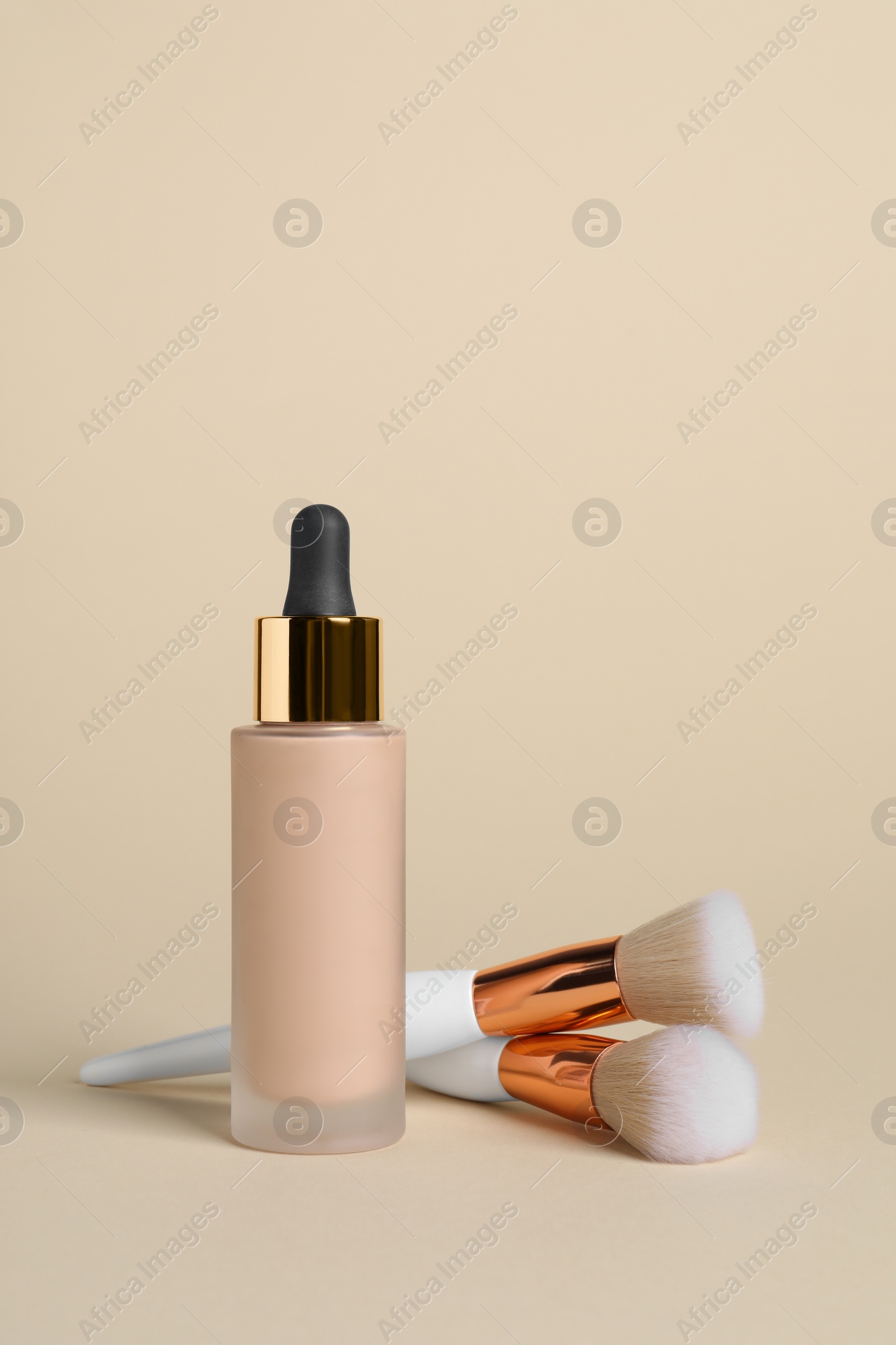 Photo of Bottle of skin foundation and brushes on beige background. Makeup product