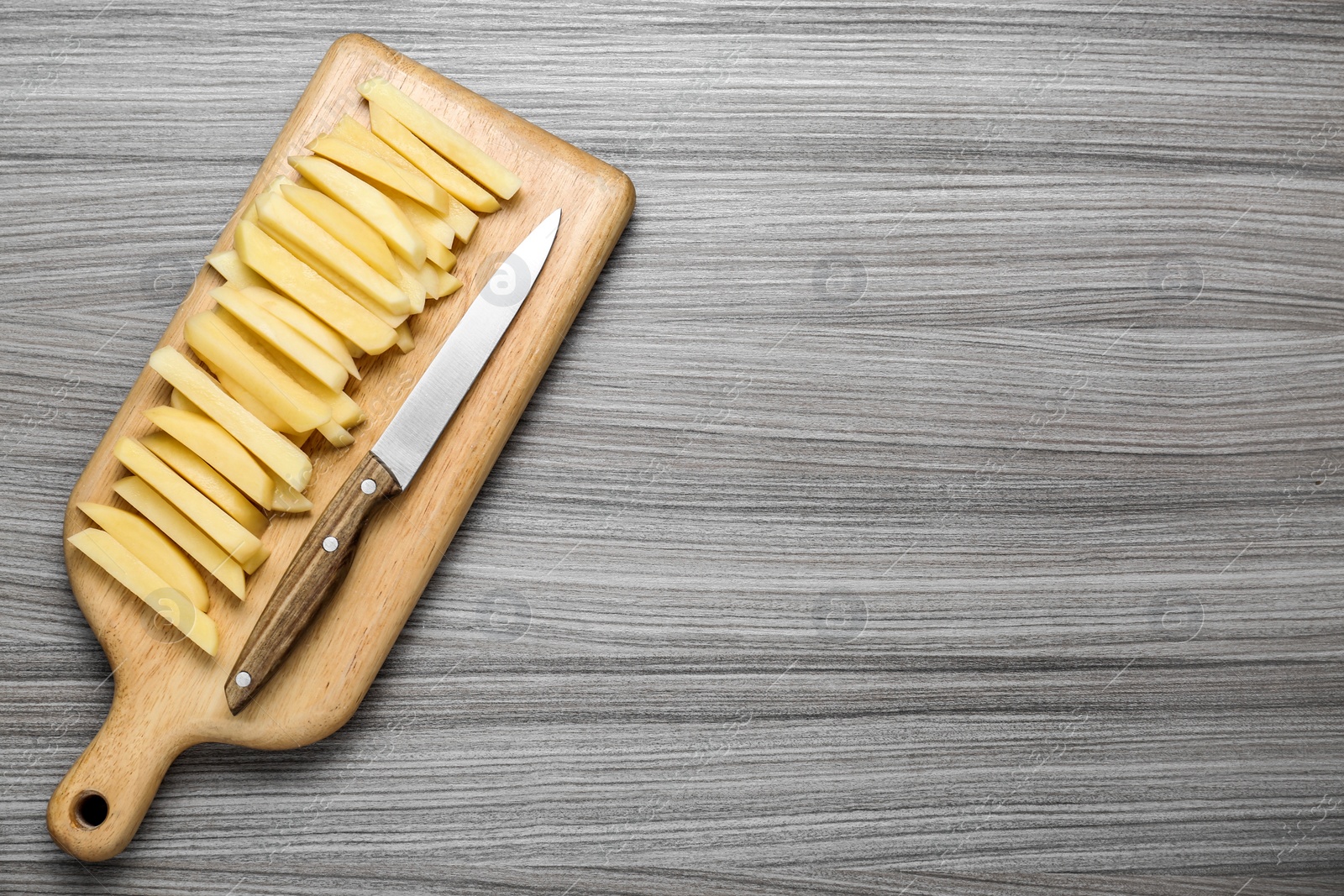 Photo of Cut raw potatoes and knife on wooden table, top view. Space for text