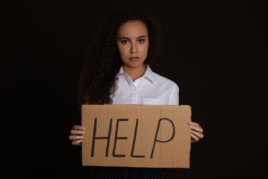 Unhappy African American woman with HELP sign on dark background
