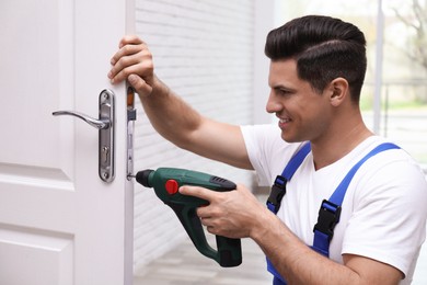 Photo of Handyman with screw gun repairing door lock indoors