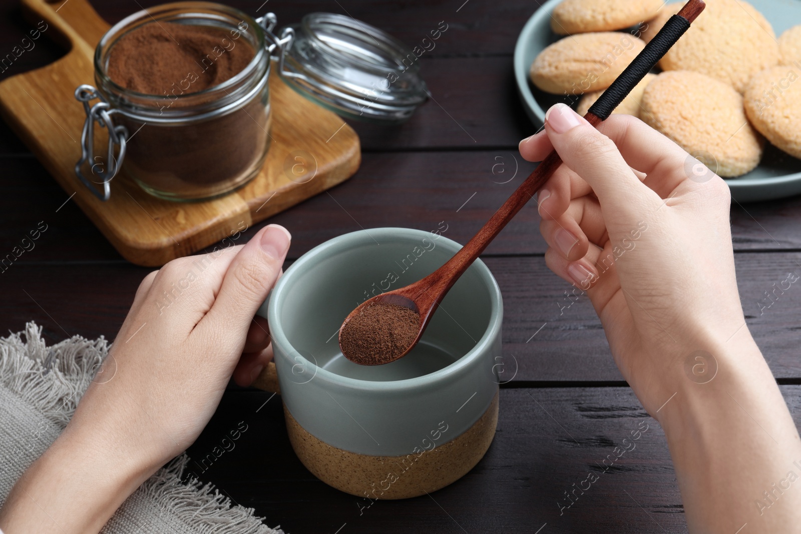 Photo of Woman pouring instant coffee into mug at wooden table, closeup