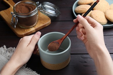 Photo of Woman pouring instant coffee into mug at wooden table, closeup