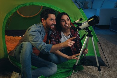 Photo of Happy couple using telescope to look at stars while sitting in camping tent indoors