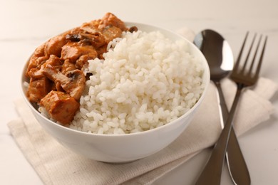 Bowl of delicious rice with meat and mushrooms on white table, closeup