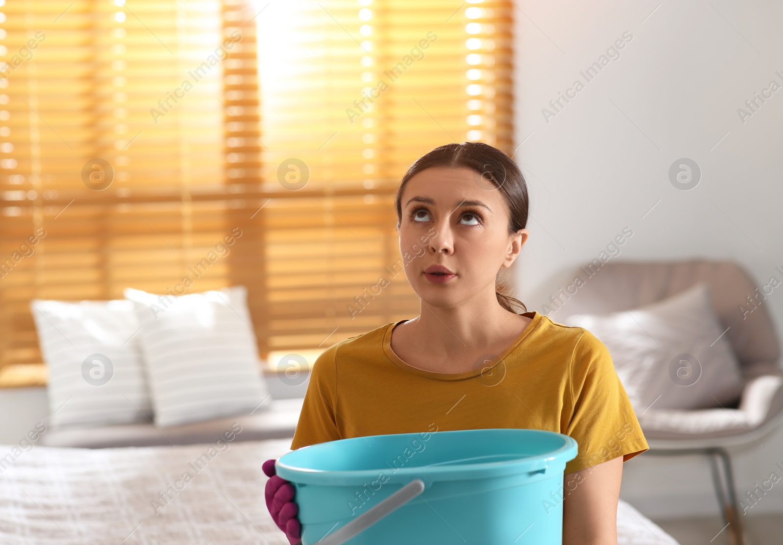 Photo of Young woman collecting leaking water from ceiling in bedroom, space for text. Time to call roof repair service