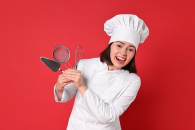Photo of Happy confectioner holding professional tools on red background