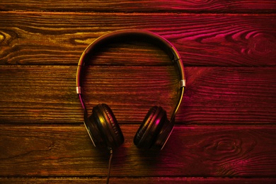 Photo of Stylish modern headphones with earmuffs on wooden background, top view