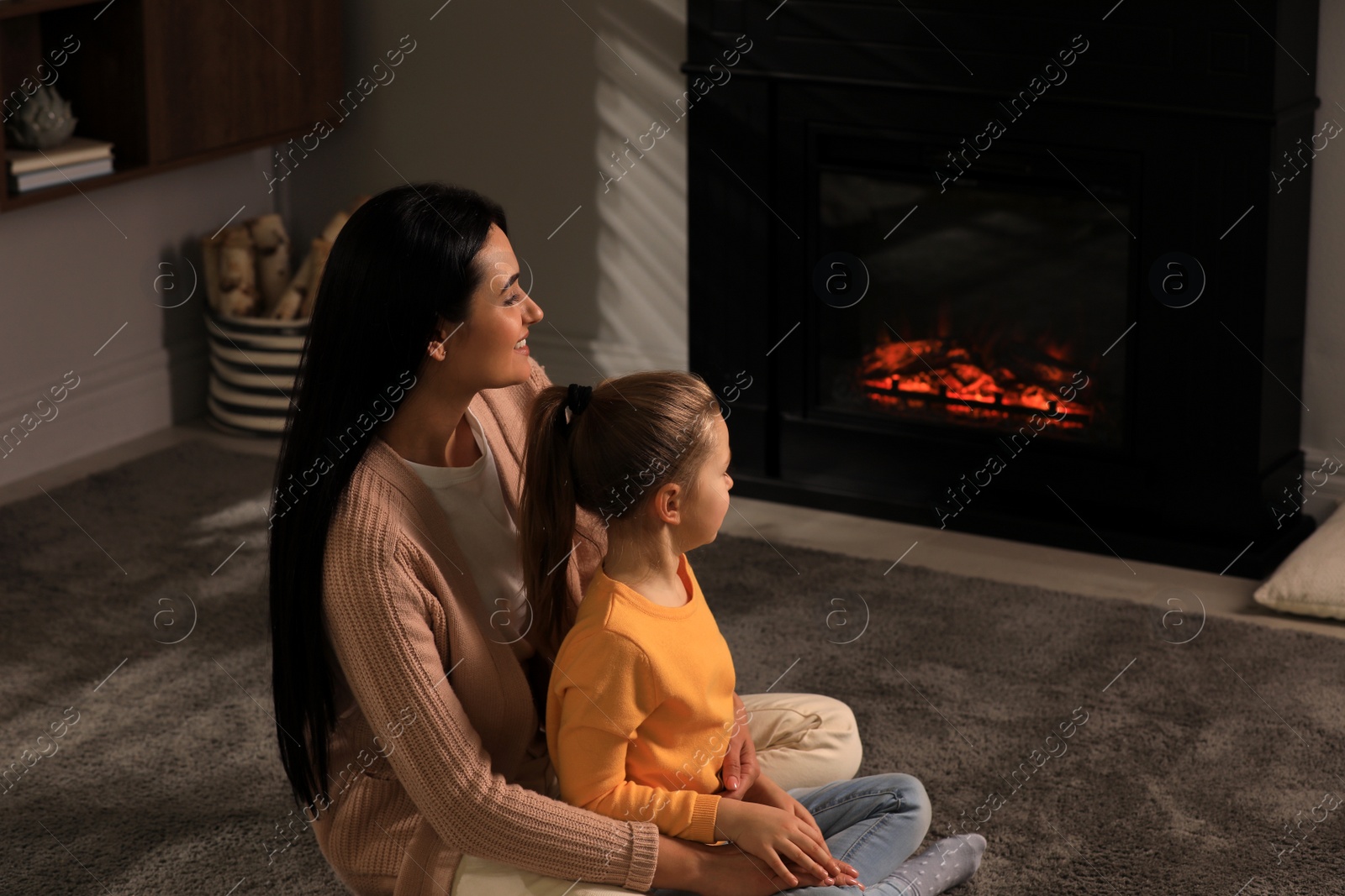 Photo of Happy mother and daughter spending time together on floor near fireplace at home