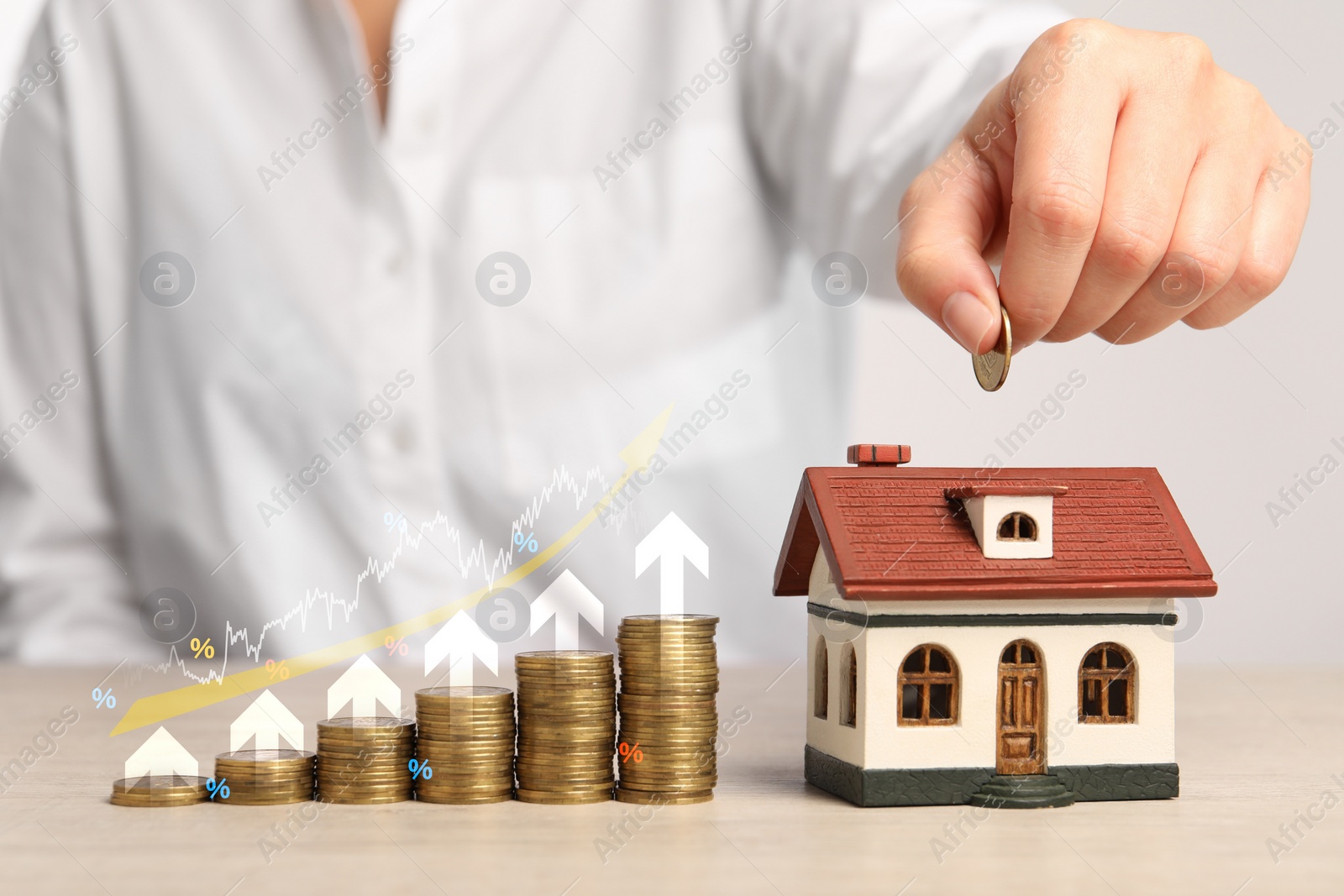 Image of Mortgage rate. Woman putting coin into house shaped money box, closeup. Stacked coins, graph, percent signs and arrows