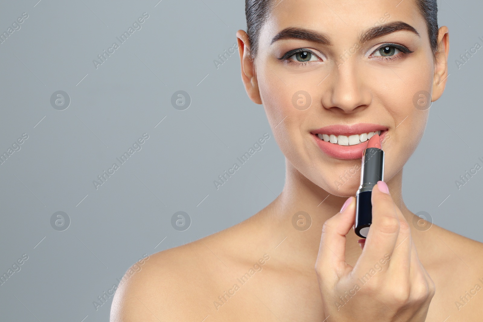 Photo of Young woman applying lipstick on color background. Space for text