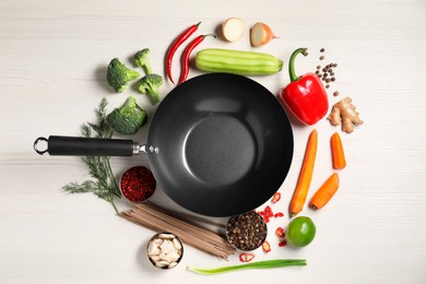 Empty iron wok surrounded by raw ingredients on white wooden table, flat lay