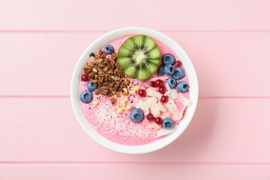 Photo of Tasty smoothie bowl with fresh kiwi fruit, berries and granola on pink wooden table, top view