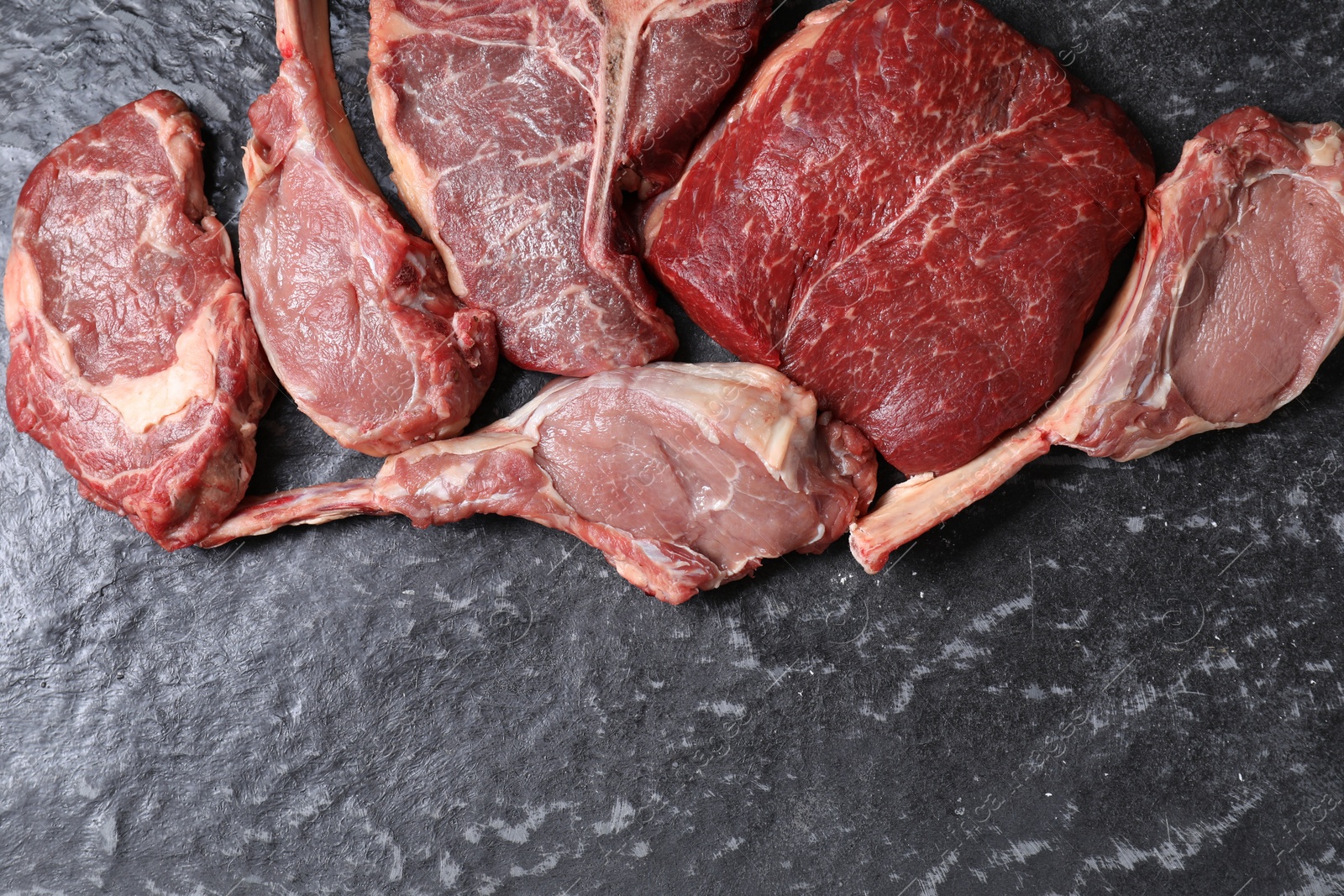 Photo of Fresh raw beef cuts on grey textured table, flat lay. Space for text