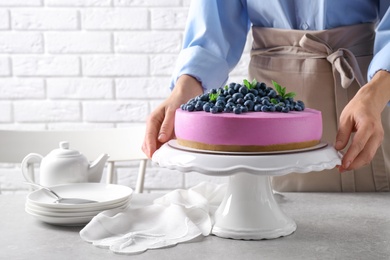 Young woman with tasty blueberry cake at grey table, closeup