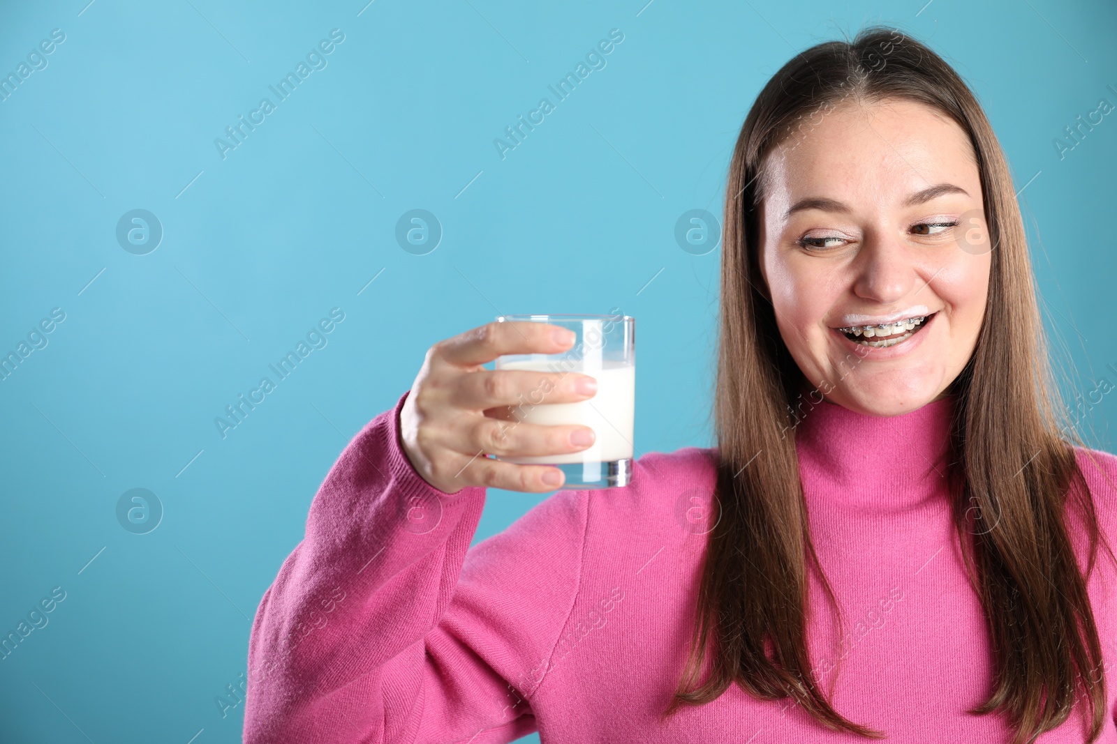 Photo of Happy woman with milk mustache holding glass of drink on light blue background. Space for text