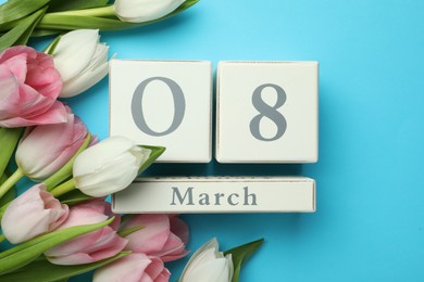 Photo of Wooden block calendar with date 8th of March and tulips on light blue background, flat lay. International Women's Day