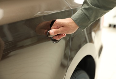 Young man opening car door in modern auto dealership, closeup