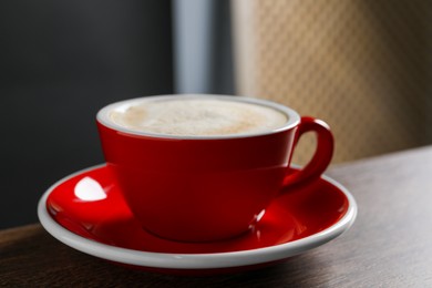 Photo of Red cup with aromatic cappuccino on wooden table indoors, closeup