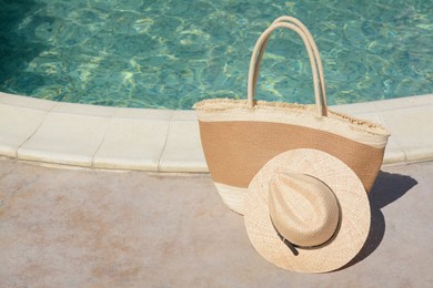 Photo of Stylish bag and hat near outdoor swimming pool on sunny day, space for text. Beach accessories