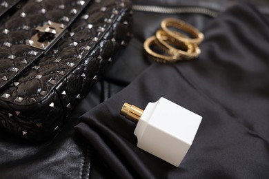 Photo of Leather bag, bottle of perfume and golden bracelets on black fabric, closeup