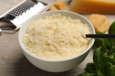 Delicious grated parmesan cheese in bowl on white wooden table, closeup