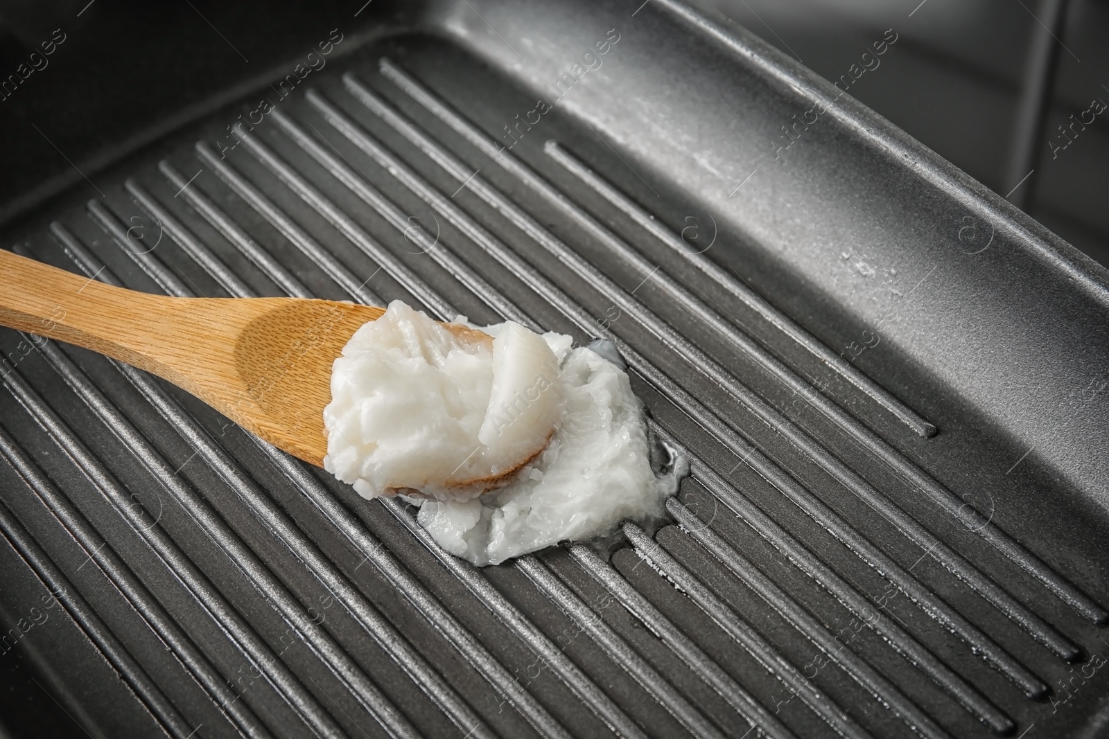 Photo of Wooden spoon with coconut oil in frying pan, closeup. Healthy cooking