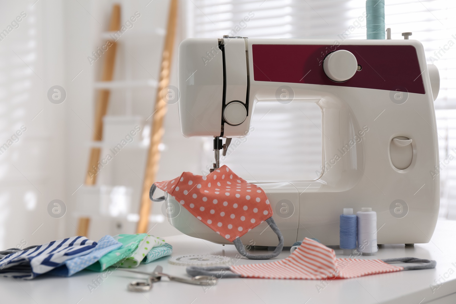 Photo of Sewing machine with cloth mask on table indoors