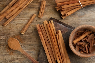 Photo of Aromatic cinnamon sticks and powder on wooden table, flat lay