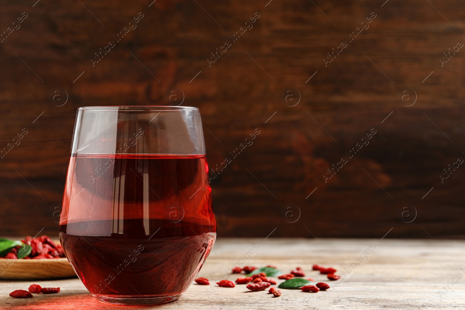 Photo of Glass of healthy goji juice on wooden table, space for text