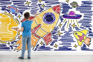 Image of Little boy drawing his dreams on wall, back view