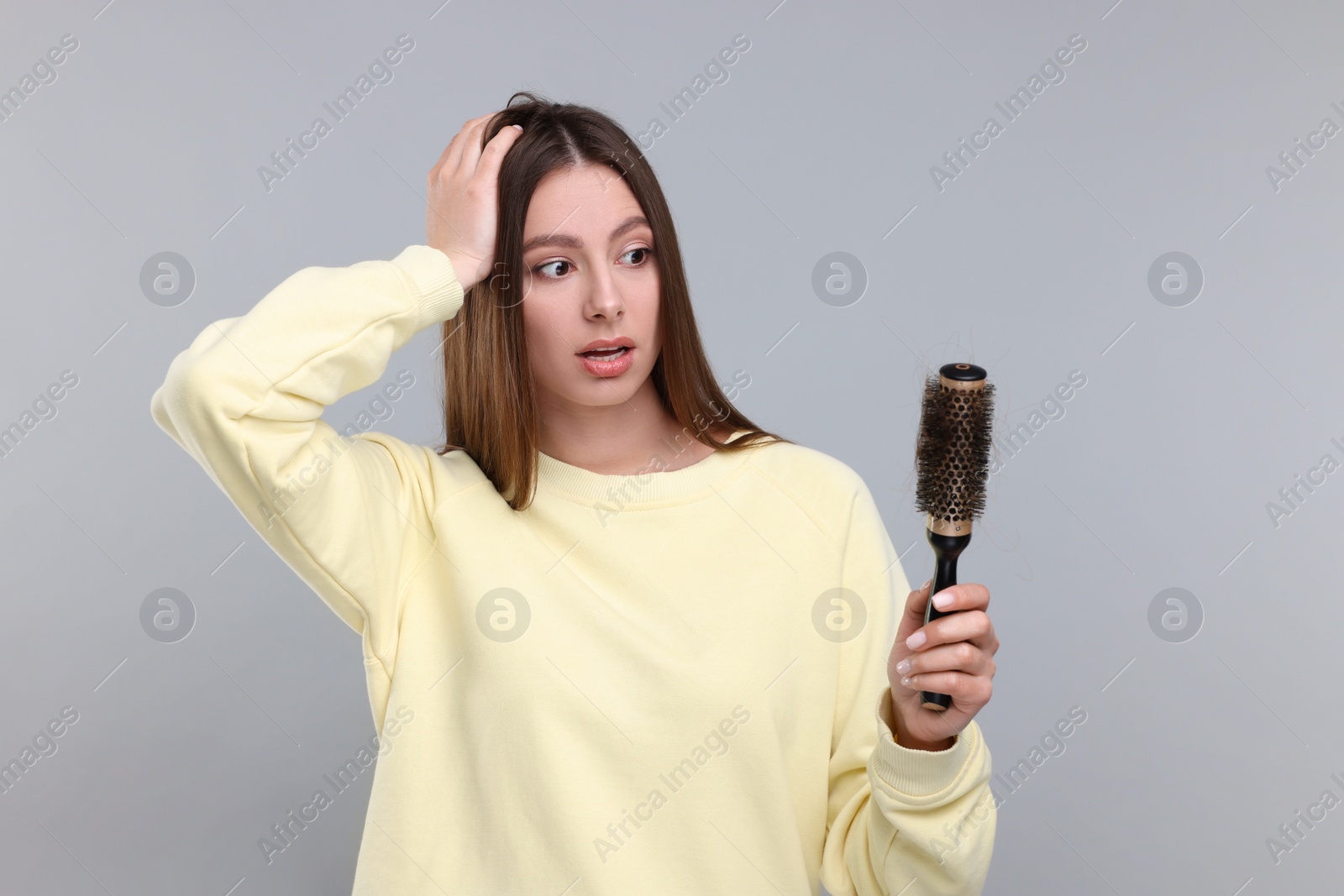 Photo of Emotional woman holding brush with lost hair on light grey background. Alopecia problem