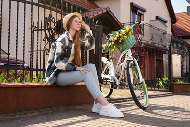 Photo of Beautiful teenage girl sitting near bicycle with bouquet of yellow tulips on city street