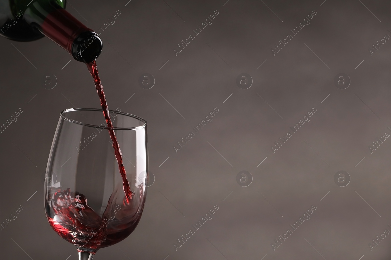 Photo of Pouring tasty red wine from bottle into glass on gray background, closeup. Space for text