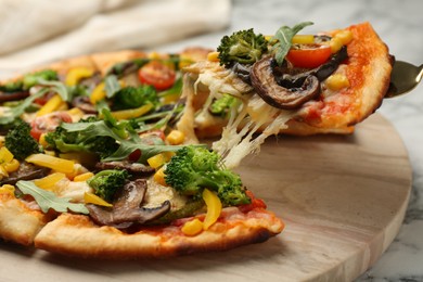 Photo of Taking piece of delicious vegetarian pizza at table, closeup