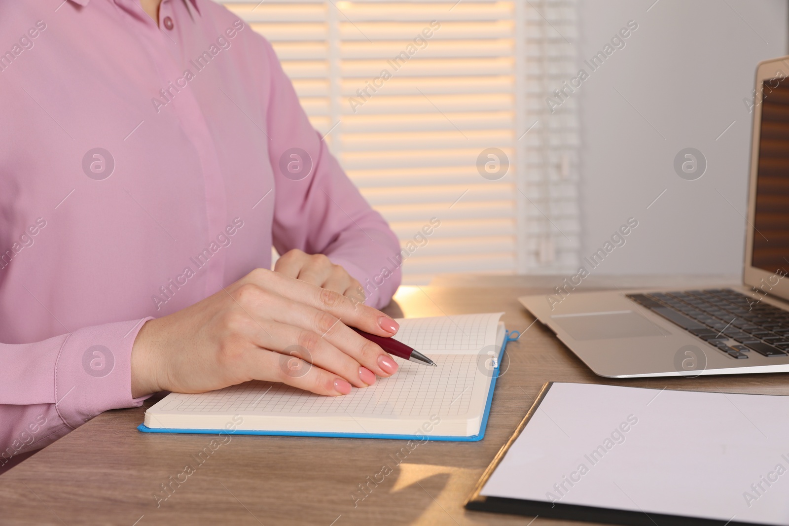 Photo of Woman taking notes at wooden table indoors, closeup. Space for text