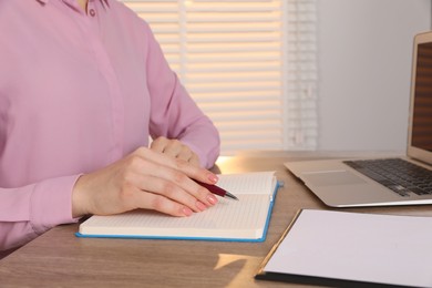 Photo of Woman taking notes at wooden table indoors, closeup. Space for text