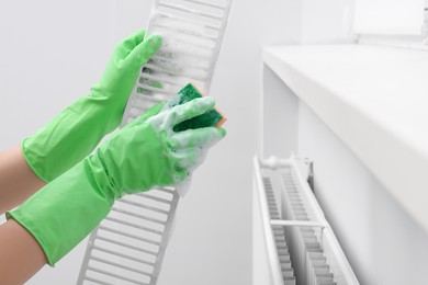 Photo of Woman washing radiator grill with sponge and detergent indoors, closeup