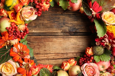 Beautiful autumnal wreath with flowers, berries and fruits on wooden background, closeup. Space for text
