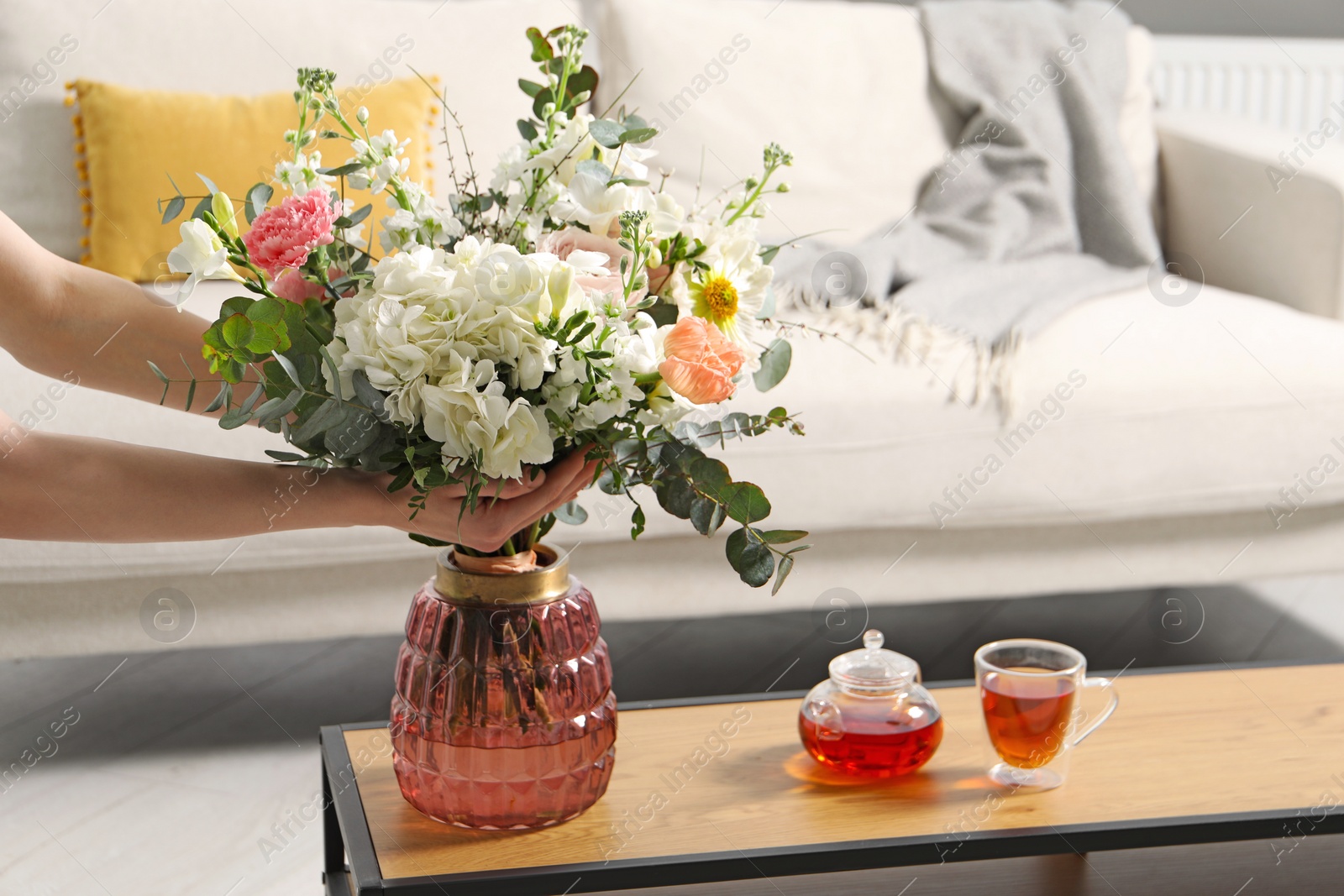 Photo of Woman arranging bouquet of beautiful flowers in vase indoors, closeup