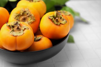 Photo of Bowl with delicious ripe juicy persimmons on white table, closeup