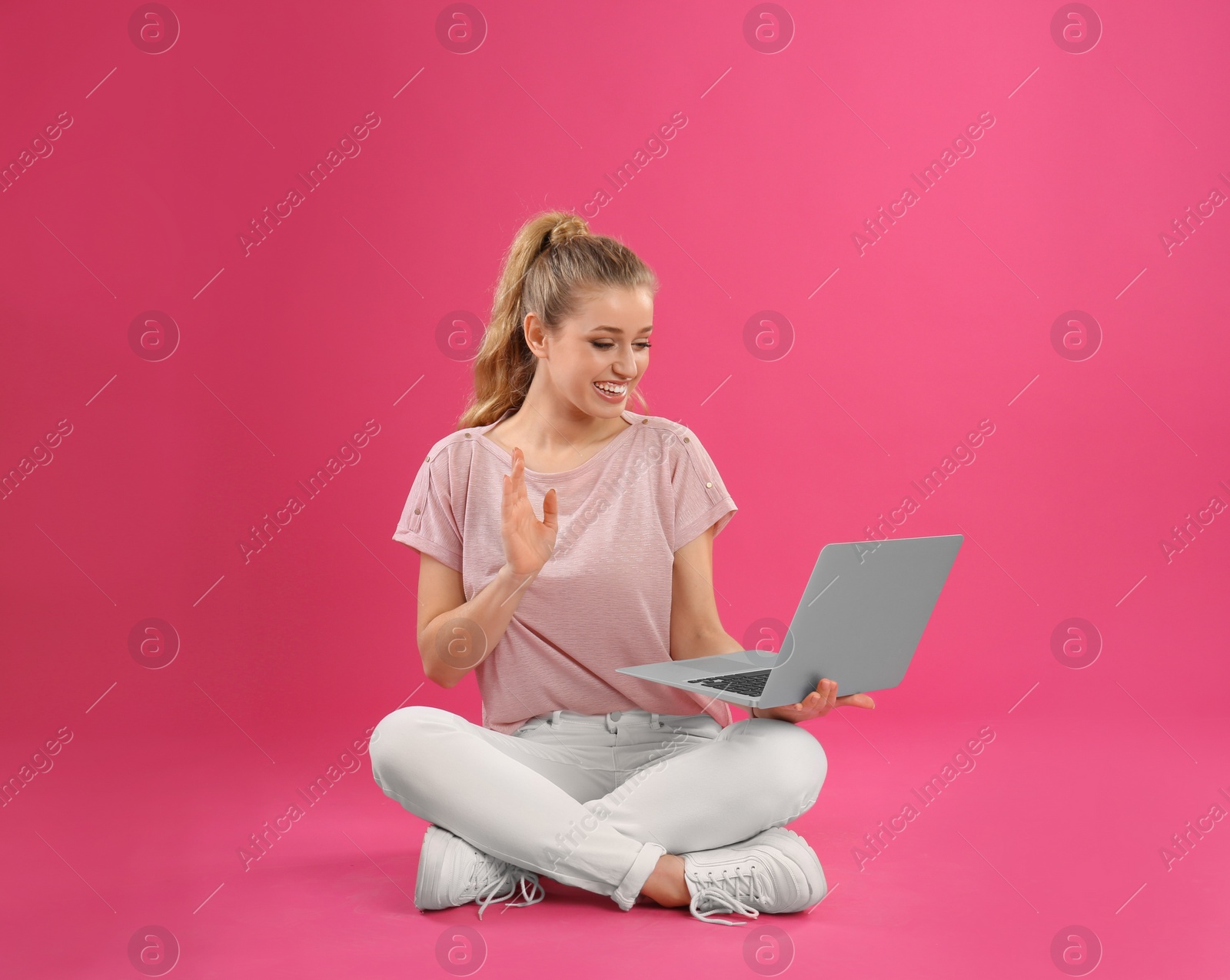 Photo of Beautiful young woman using laptop on pink background