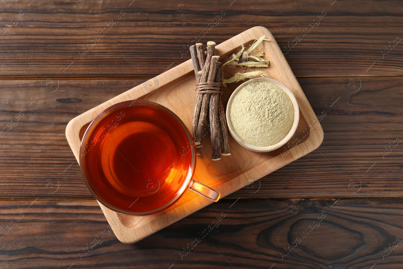 Photo of Aromatic licorice tea in cup, dried sticks of licorice root and powder on wooden table, top view