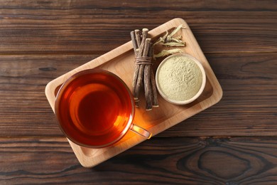 Aromatic licorice tea in cup, dried sticks of licorice root and powder on wooden table, top view