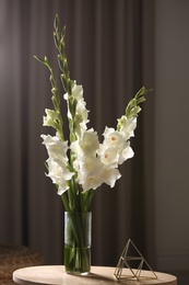 Photo of Vase with beautiful white gladiolus flowers on wooden table in room