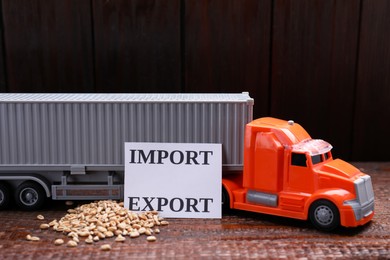 Photo of Card with words Import and Export near toy truck and wheat grains on wooden table