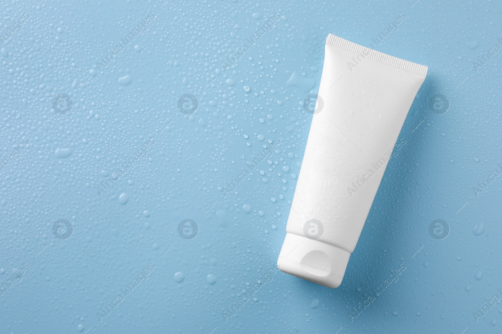 Photo of Moisturizing cream in tube on light blue background with water drops, top view. Space for text