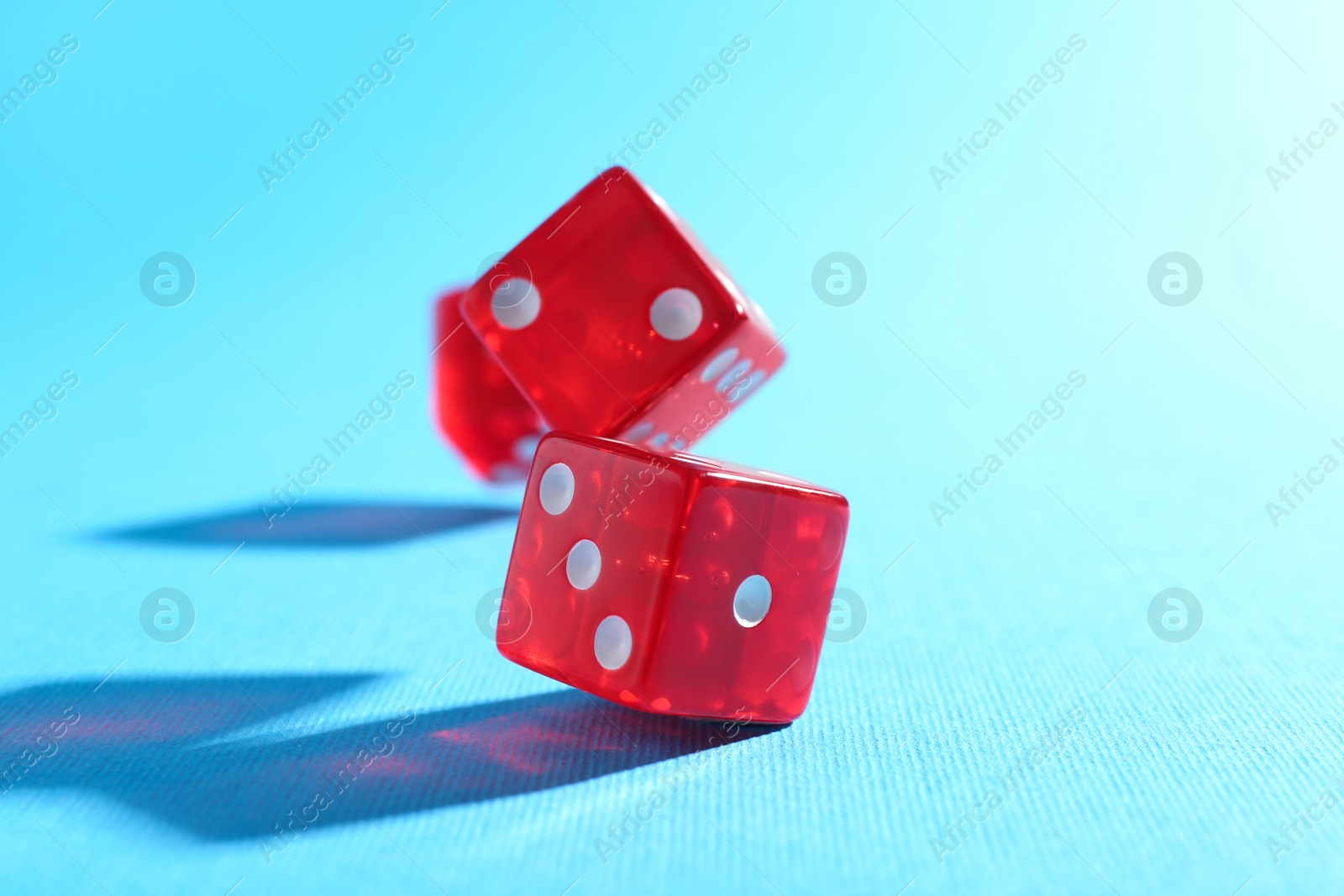 Photo of Three red game dices falling on light blue background, closeup