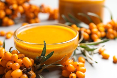 Delicious sea buckthorn jam and fresh berries on light grey table, closeup